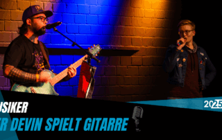 Devin spielt auf seiner Gitarre und wird von einem Sänger begleitet.